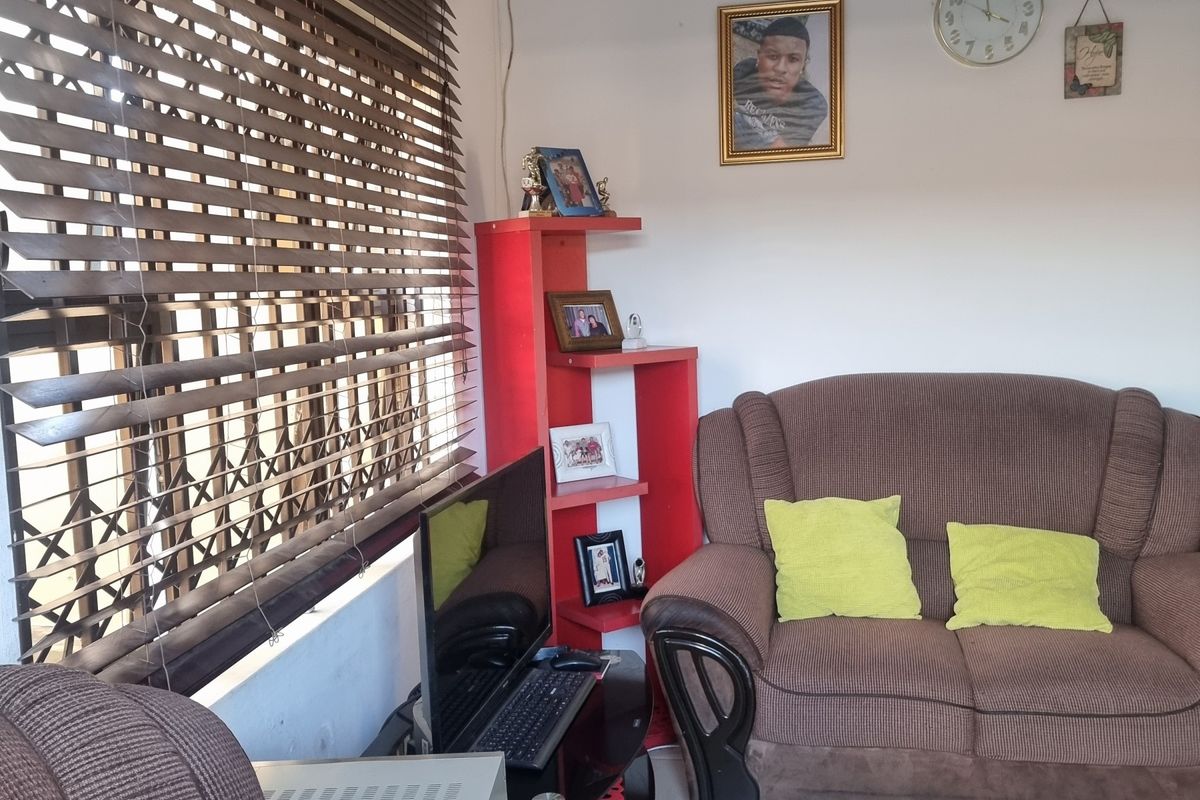 A functional living room featuring tiled flooring and large windows fitted with venetian blinds and security gates.