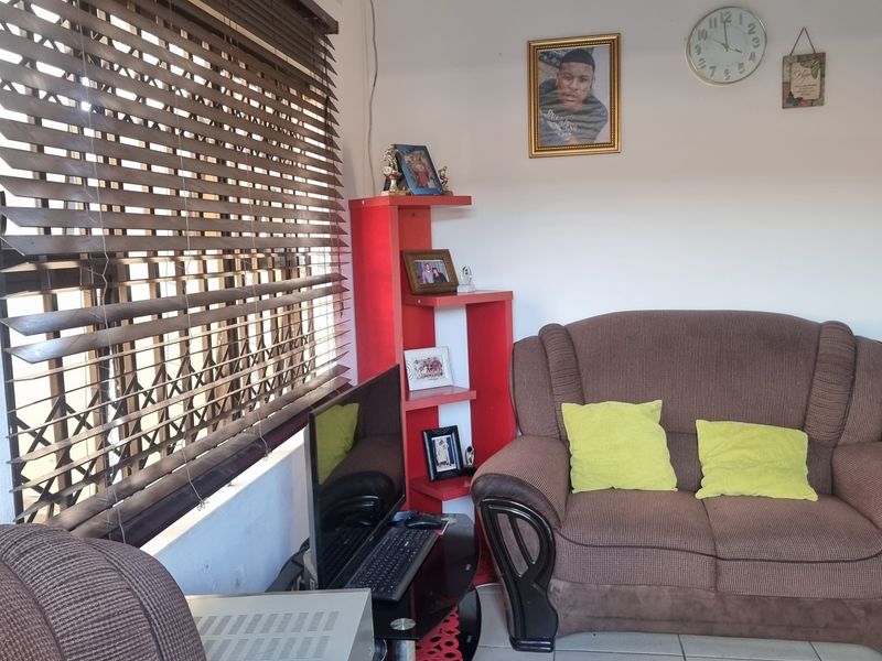 A functional living room featuring tiled flooring and large windows fitted with venetian blinds and security gates.