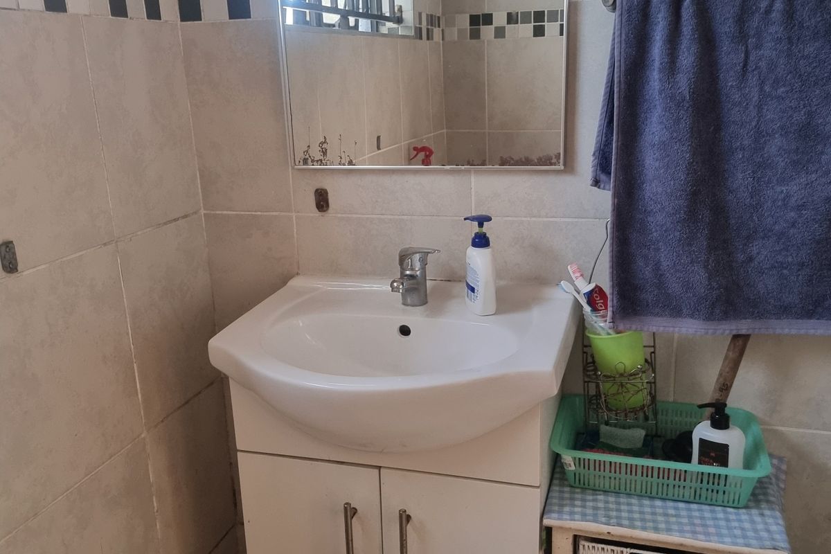 A functional bathroom featuring a vanity cabinet with a ceramic basin, wall-mounted mirror, and tiled walls with a decorative border.