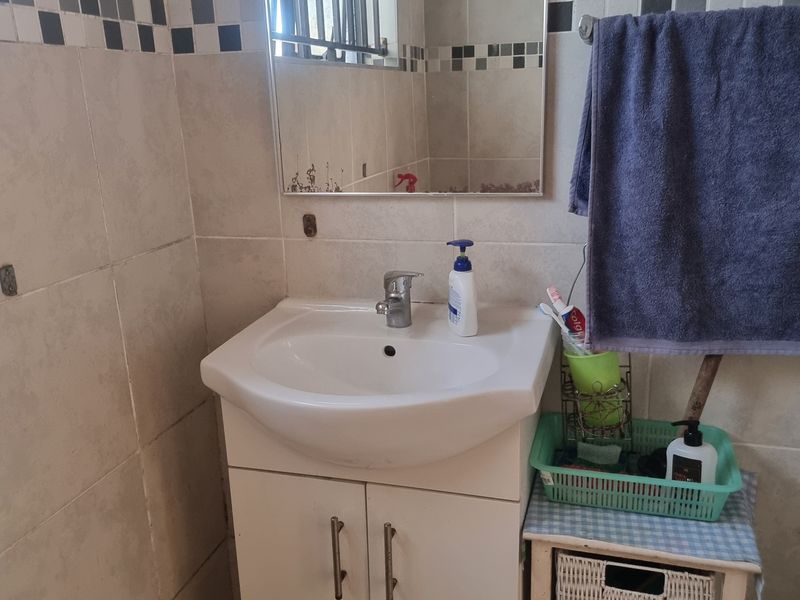 A functional bathroom featuring a vanity cabinet with a ceramic basin, wall-mounted mirror, and tiled walls with a decorative border.