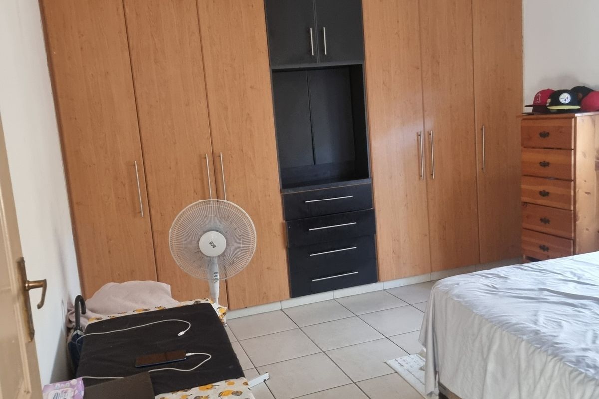 A bedroom featuring extensive built-in wooden cabinetry with integrated shelving and drawers, tiled flooring, and a wall-mounted air conditioning unit.