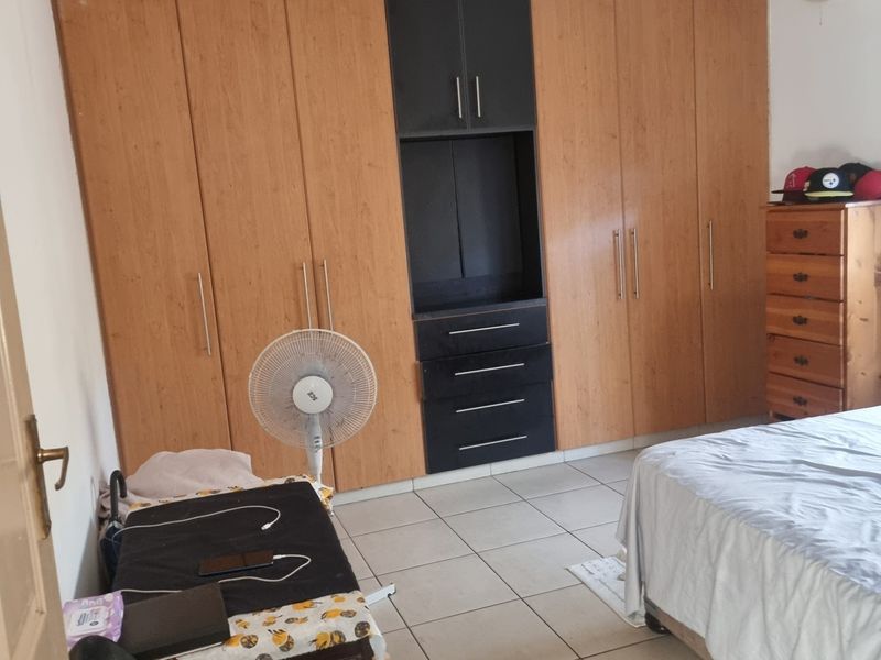 A bedroom featuring extensive built-in wooden cabinetry with integrated shelving and drawers, tiled flooring, and a wall-mounted air conditioning unit.