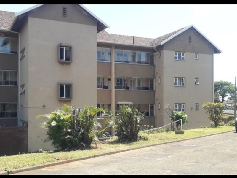 Exterior view of a multi-story apartment complex featuring a tiled roof, casement windows, and a paved driveway with surrounding garden area.