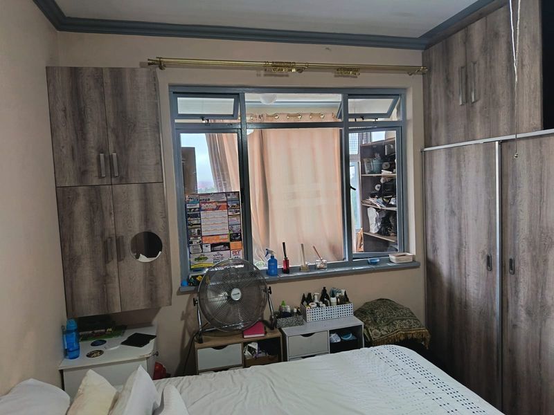 A bedroom featuring built-in wooden cupboards and an aluminium-framed window with a curtain rod.