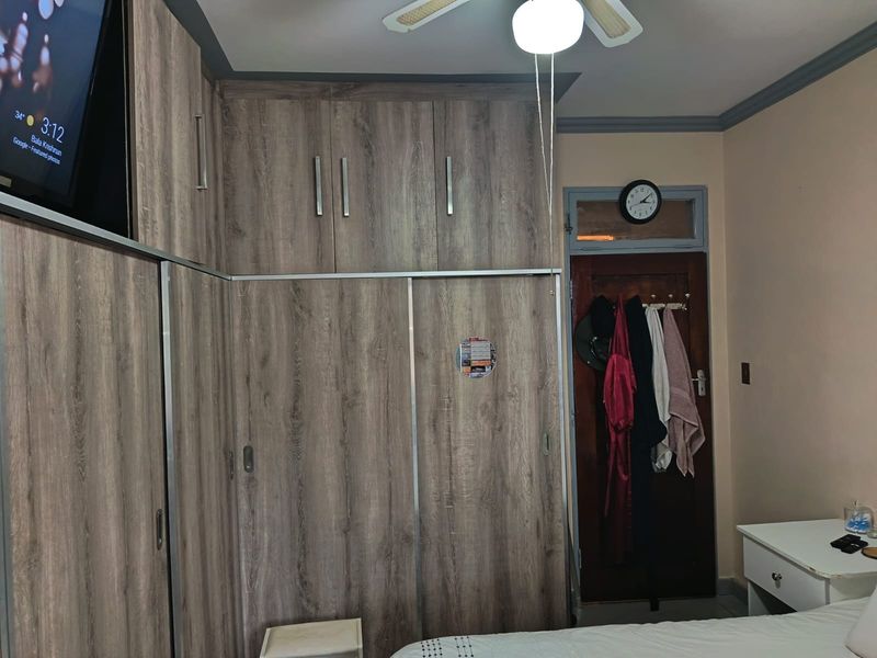 A bedroom featuring extensive wood-grain built-in cupboards, a ceiling fan, and a traditional timber door with a transom window.