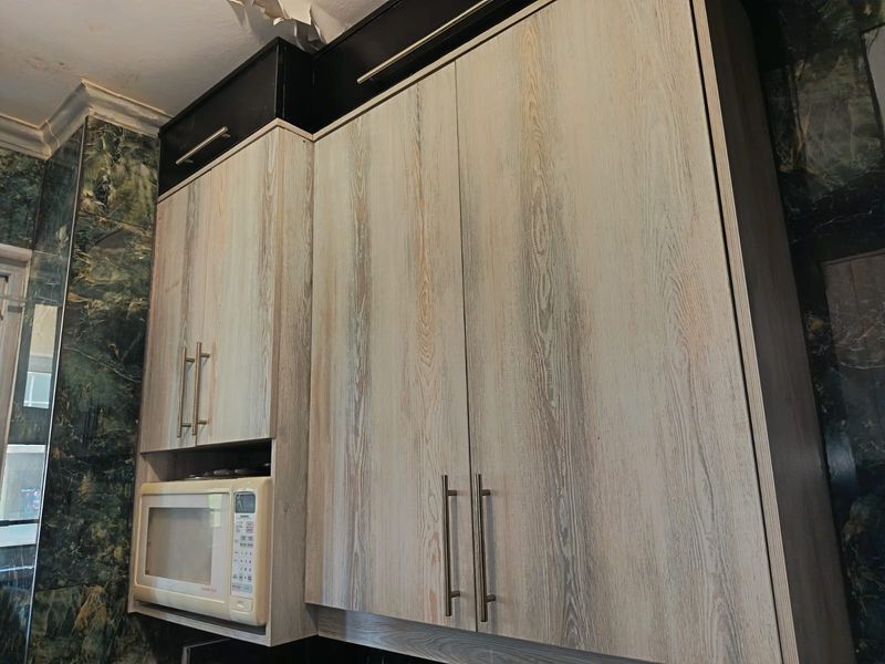 Close-up view of kitchen cabinetry with built-in microwave and decorative wall tiling, showing visible ceiling damage requiring repair.