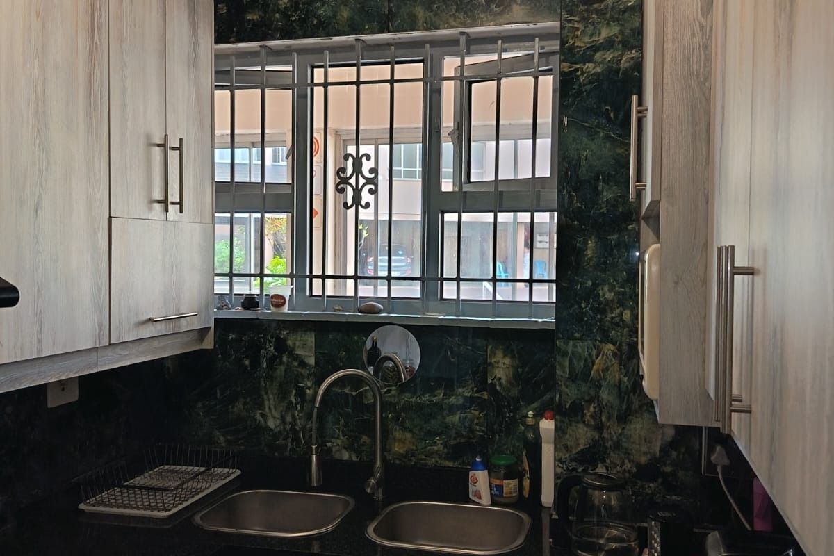 Compact kitchen featuring granite countertops, double stainless steel sink, and modern laminate cabinetry with a tiled splashback.