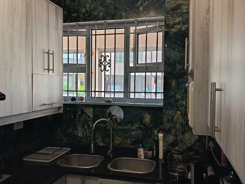 Compact kitchen featuring granite countertops, double stainless steel sink, and modern laminate cabinetry with a tiled splashback.