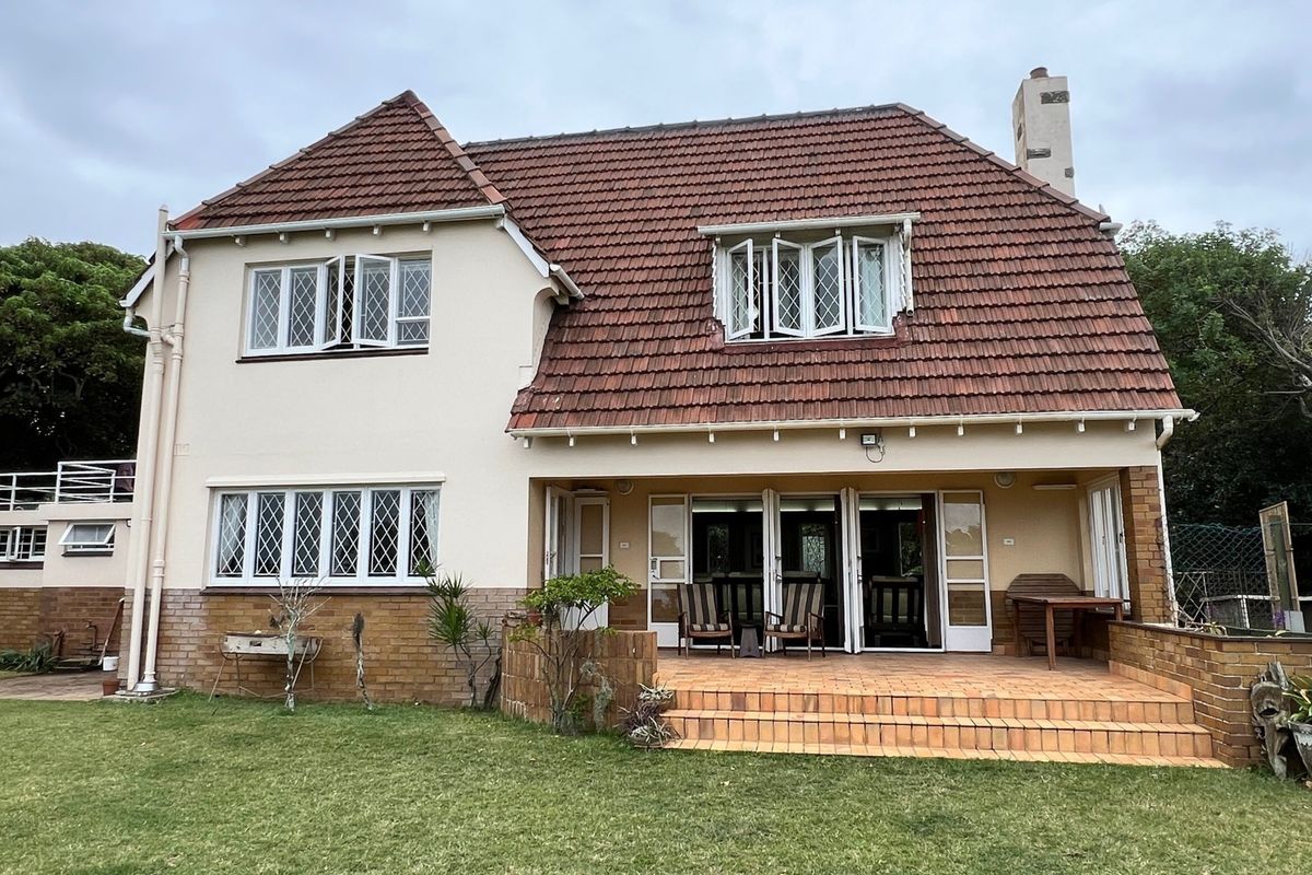 Rear view of a two-story house featuring a tiled roof, brick facade, leaded glass windows, and a paved patio area overlooking the garden.