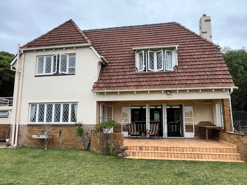 Rear view of a two-story house featuring a tiled roof, brick facade, leaded glass windows, and a paved patio area overlooking the garden.