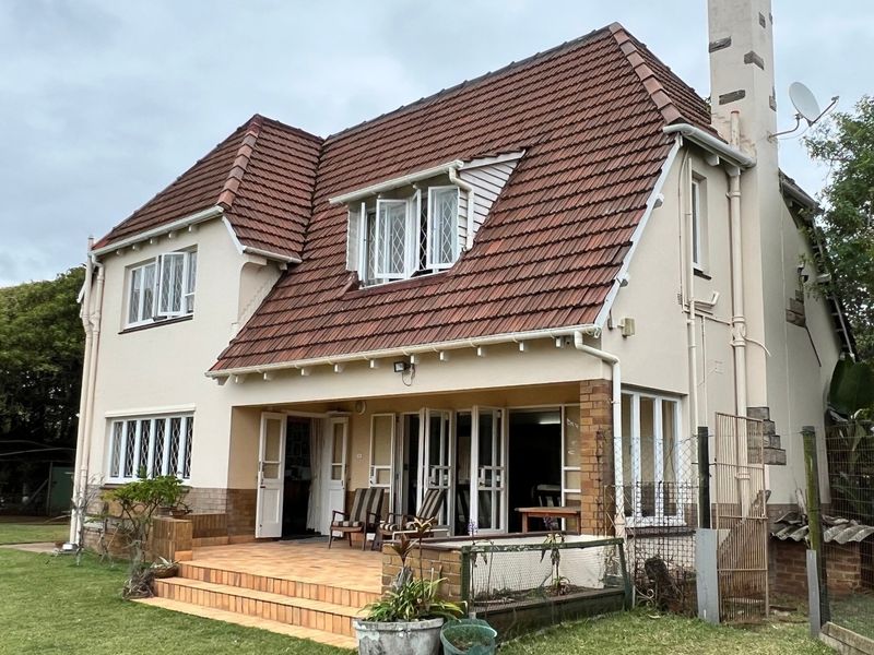 Rear view of a two-story house featuring a tiled roof, brick chimney, and a covered patio area leading out to the garden.