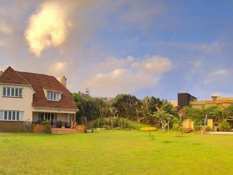 A panoramic view of the rear elevation of the house, featuring a spacious garden, a terrace, and a swimming pool area.