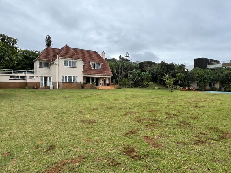 Rear view of a traditional two-story house featuring a tiled roof, brick accents, and a spacious garden with an adjacent swimming pool area.