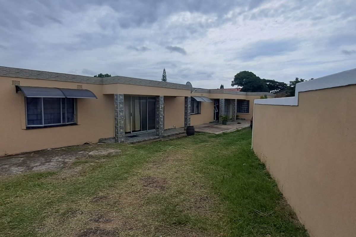 Rear view of the property featuring a concrete patio, sliding glass doors, and a surrounding boundary wall with a lawn area.