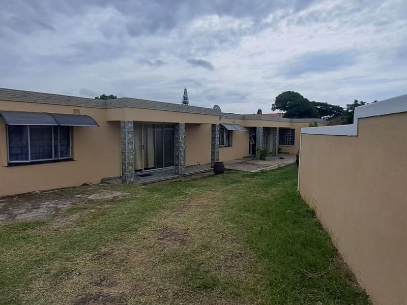Rear view of the property featuring a concrete patio, sliding glass doors, and a surrounding boundary wall with a lawn area.
