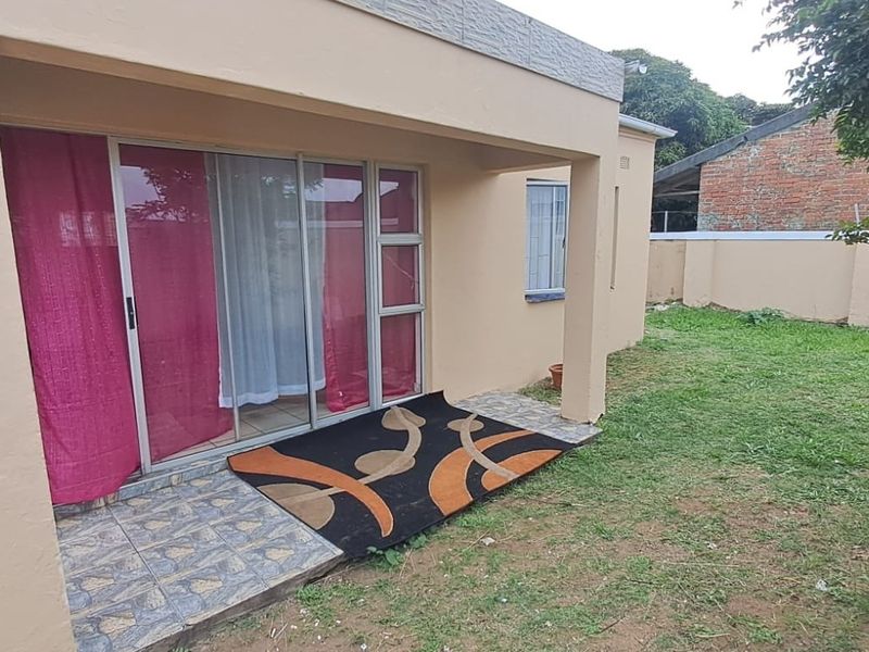 A covered patio area featuring tiled flooring and a sliding glass door entrance, overlooking a private garden space.