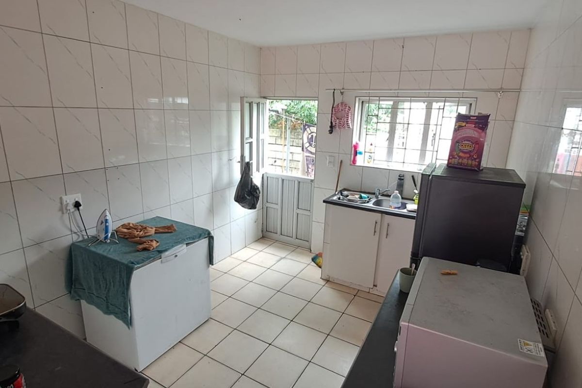 A functional kitchen space featuring tiled walls and flooring, built-in cabinetry, and a sink, with direct access to the exterior via a security gate.