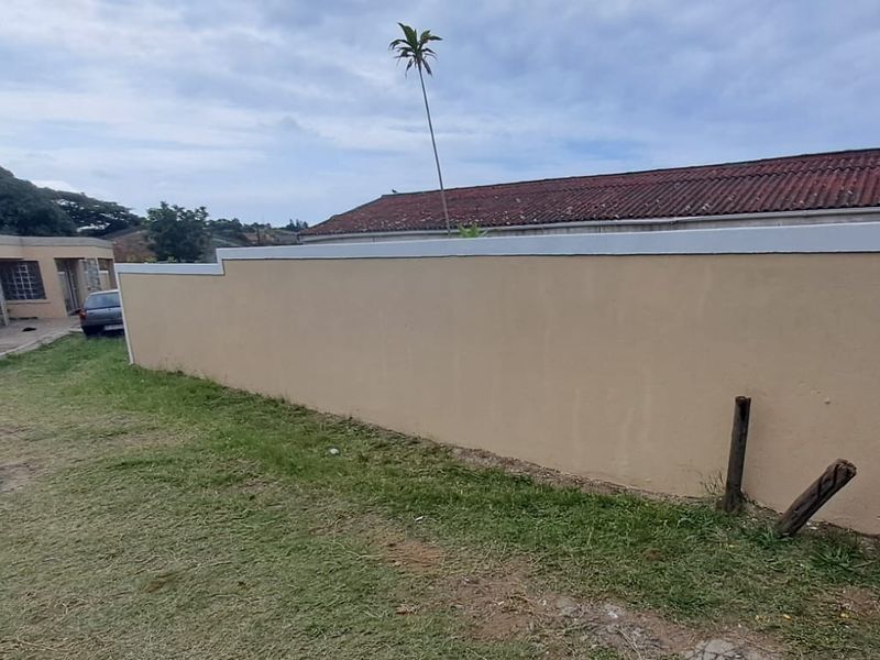 A view of the rear garden area featuring a painted boundary wall and a grass lawn.