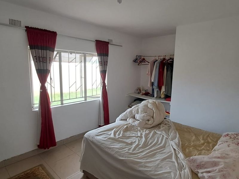 A functional bedroom featuring tiled flooring, built-in shelving, and security bars on the window, offering a basic layout ready for cosmetic updates.