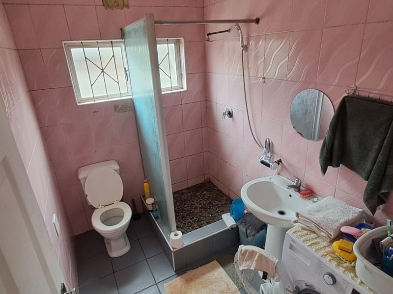 A functional bathroom featuring a walk-in shower, pedestal basin, and toilet, finished with dated pink wall tiles and floor tiling.