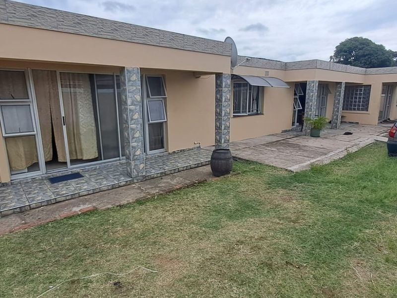 Rear exterior view of the house featuring a tiled patio area, stone-clad pillars, sliding glass doors, and a spacious lawn.