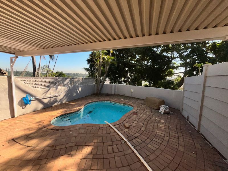 A private outdoor pool area featuring brick paving, a covered patio structure, and boundary walls, offering a functional space for relaxation.