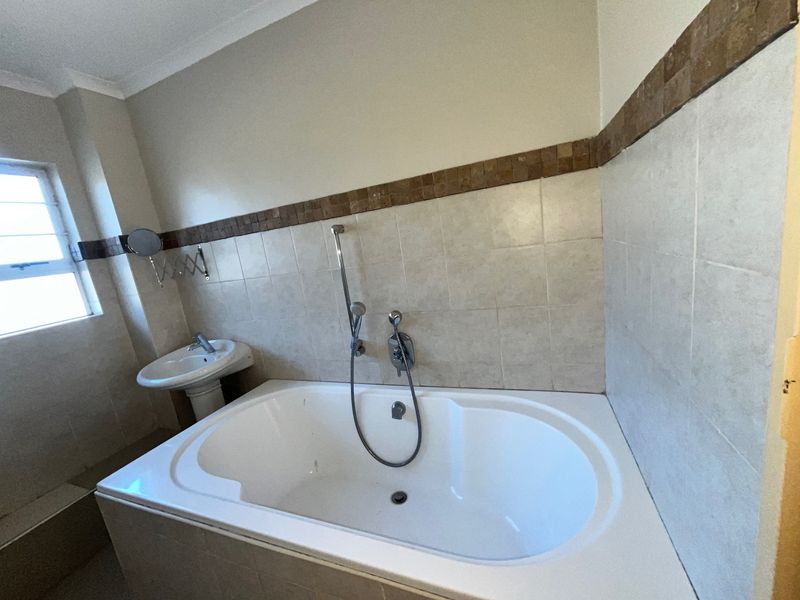 A functional bathroom featuring a built-in bathtub with a handheld shower attachment and a pedestal basin, finished with neutral wall tiling.