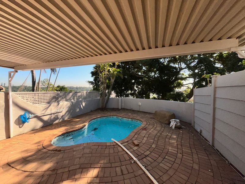 Outdoor pool area featuring a covered patio, brick paving, and boundary walls, offering a private space for relaxation and outdoor entertainment.