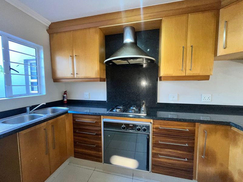 A functional kitchen featuring wooden cabinetry, granite countertops, a built-in gas hob, oven, and stainless steel extractor fan with tiled flooring.
