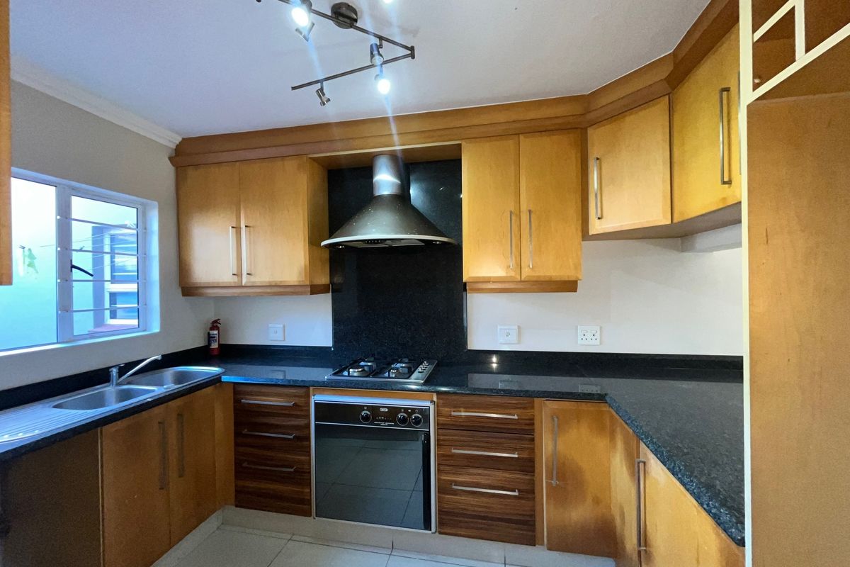 A functional kitchen featuring wooden cabinetry, granite countertops, a built-in oven with gas hob, and an extractor fan.