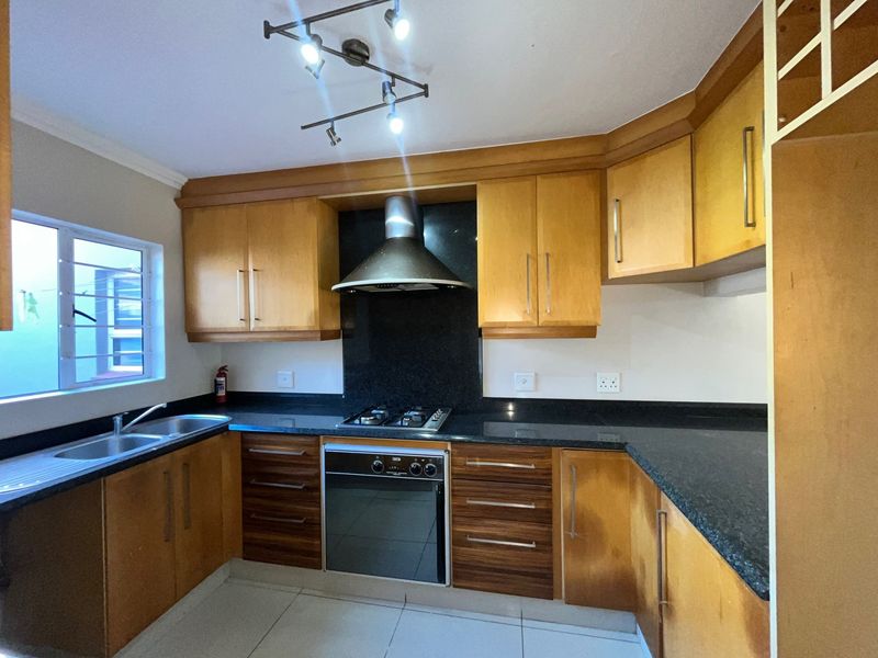 A functional kitchen featuring wooden cabinetry, granite countertops, a built-in oven with gas hob, and an extractor fan.