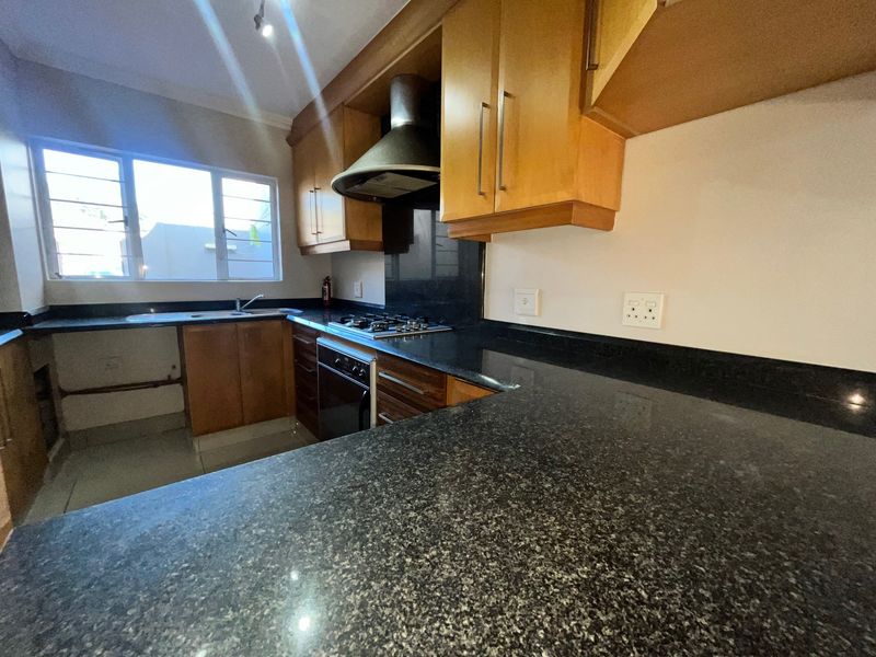 A functional kitchen featuring granite countertops, wooden cabinetry, a built-in oven with gas hob, and an extractor fan.