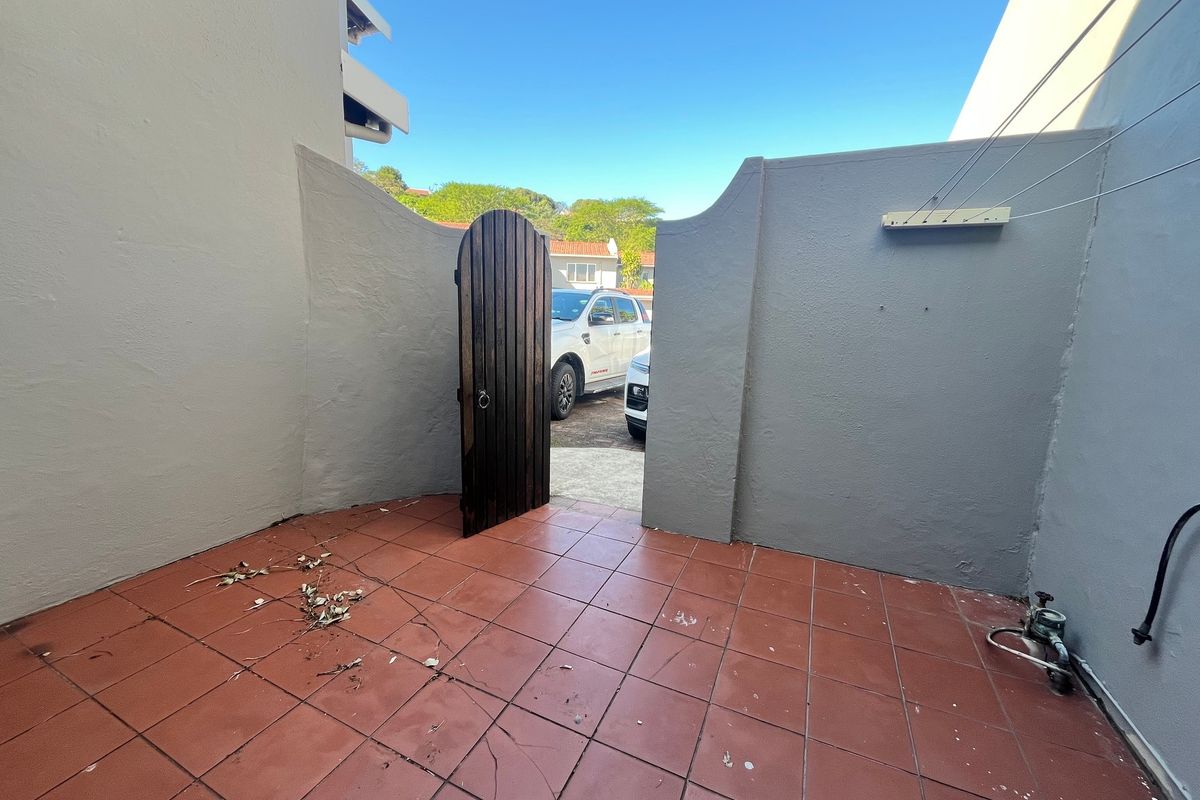 A small, paved outdoor courtyard area featuring a wooden gate, boundary walls, and a wall-mounted clothesline.