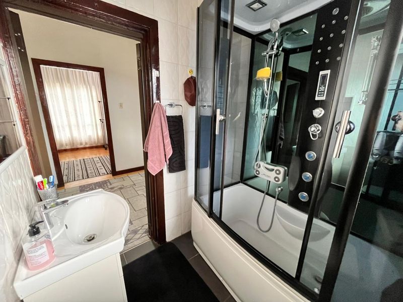 A functional bathroom featuring a modern enclosed shower cabin with integrated jets and a pedestal washbasin, finished with tiled walls and flooring.