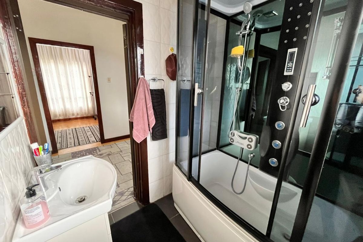 A functional bathroom featuring a modern enclosed shower cabin with integrated jets and a pedestal washbasin, finished with tiled walls and flooring.