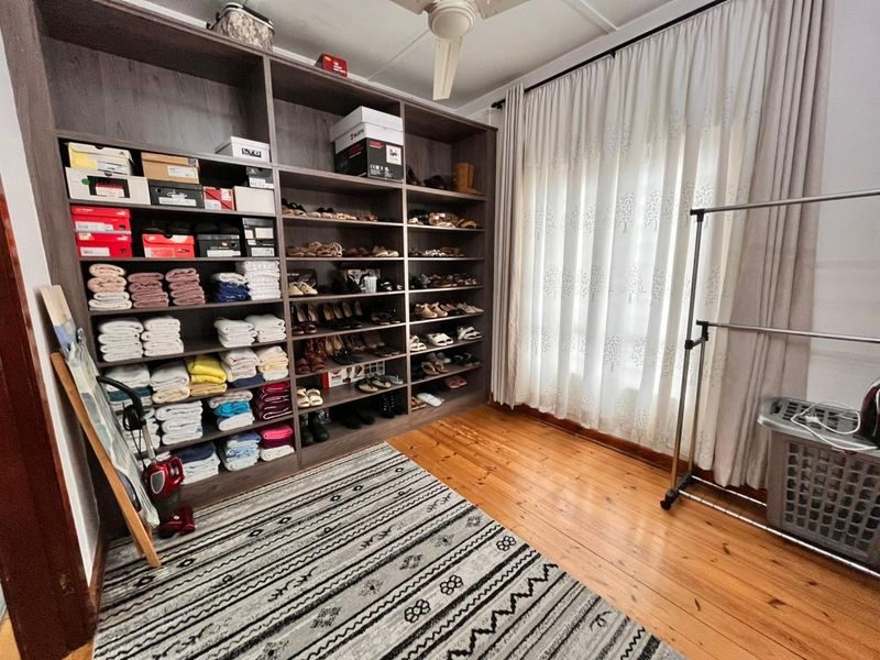 A bedroom featuring polished timber flooring, a ceiling fan, and extensive built-in floor-to-ceiling shelving units for storage.