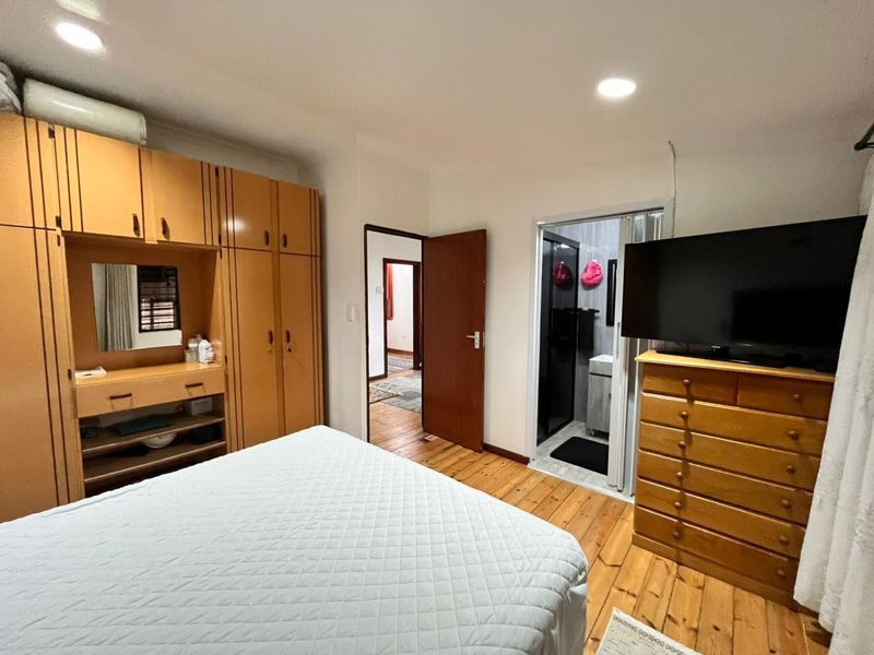 A bedroom featuring timber flooring, built-in cabinetry, and recessed lighting, with an adjoining en-suite bathroom visible through a folding door.