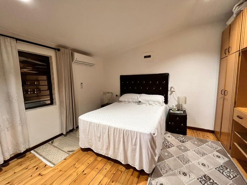 A bedroom featuring polished timber flooring, a built-in wardrobe, and a wall-mounted split-system air conditioning unit.