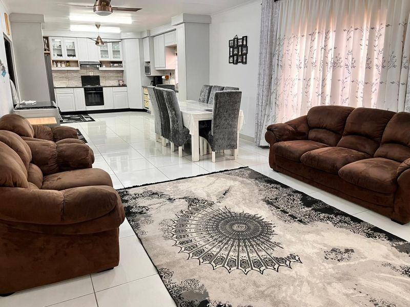 Spacious open-plan living and dining area featuring modern white kitchen cabinetry, integrated appliances, and polished tiled flooring throughout.