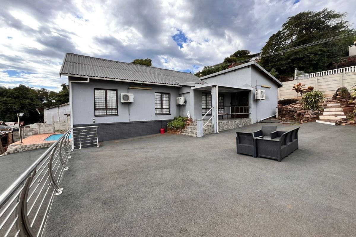 Rear exterior view of the house featuring a large asphalt driveway, stainless steel balustrades, and multiple wall-mounted air conditioning units.