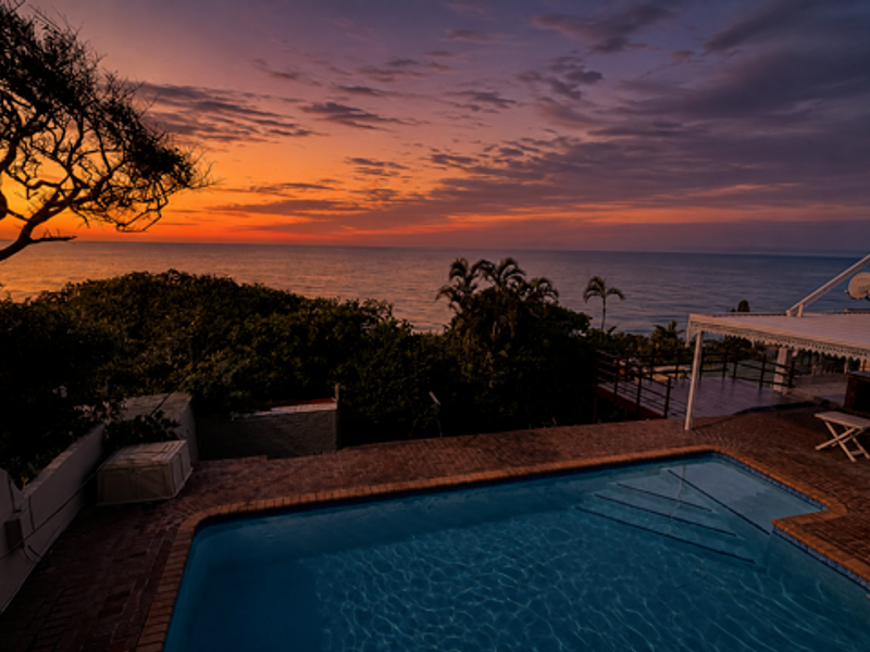 Outdoor pool area featuring a swimming pool, covered patio, and stunning sunset ocean views.