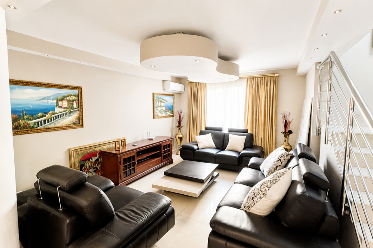 A well-maintained living room featuring tiled flooring, recessed ceiling lighting, a split-system air conditioner, and a modern staircase with a stainless steel railing.
