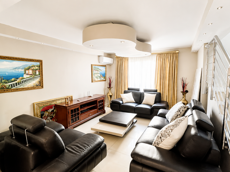 A well-maintained living room featuring tiled flooring, recessed ceiling lighting, a split-system air conditioner, and a modern staircase with a stainless steel railing.