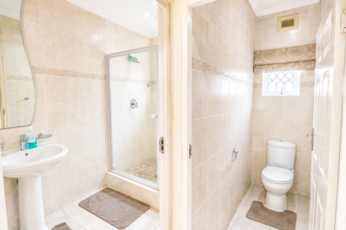 A functional bathroom featuring a pedestal basin, a separate shower enclosure, and a toilet, finished with neutral wall and floor tiles.