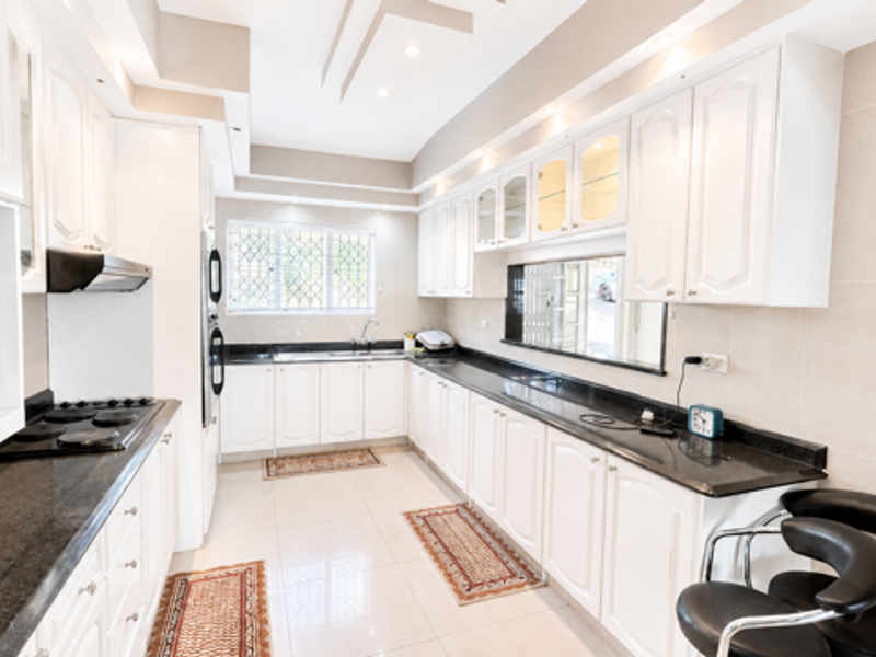 A well-maintained kitchen featuring white cabinetry, dark granite countertops, integrated appliances, recessed lighting, and neutral tiled finishes throughout.
