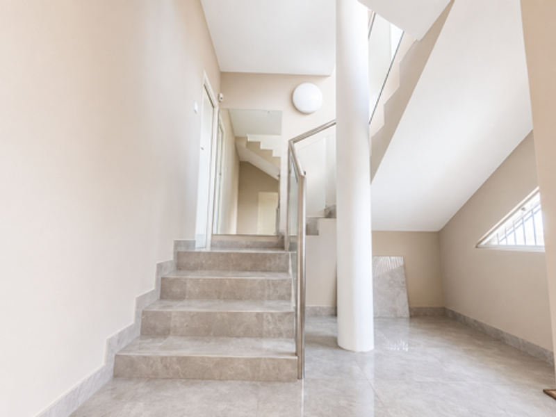 Modern entrance foyer featuring a tiled staircase with a glass balustrade, stainless steel handrail, and clean neutral finishes.
