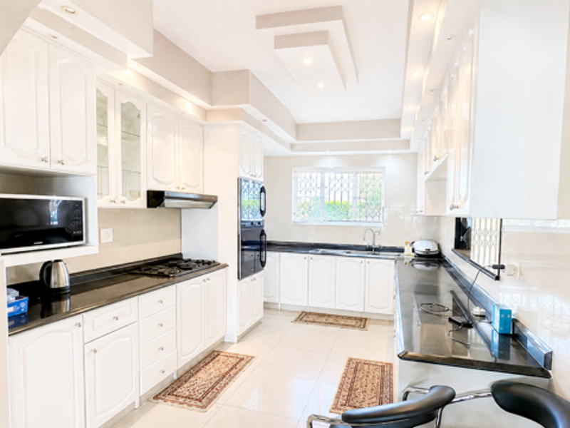 A spacious, well-lit kitchen featuring white cabinetry, granite countertops, integrated appliances, and modern recessed ceiling lighting.