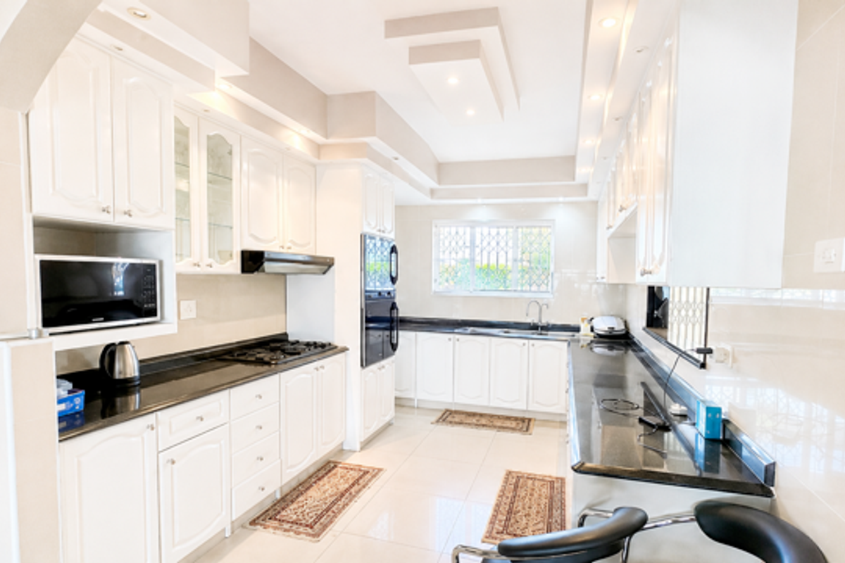 A spacious, well-lit kitchen featuring white cabinetry, granite countertops, integrated appliances, and modern recessed ceiling lighting.