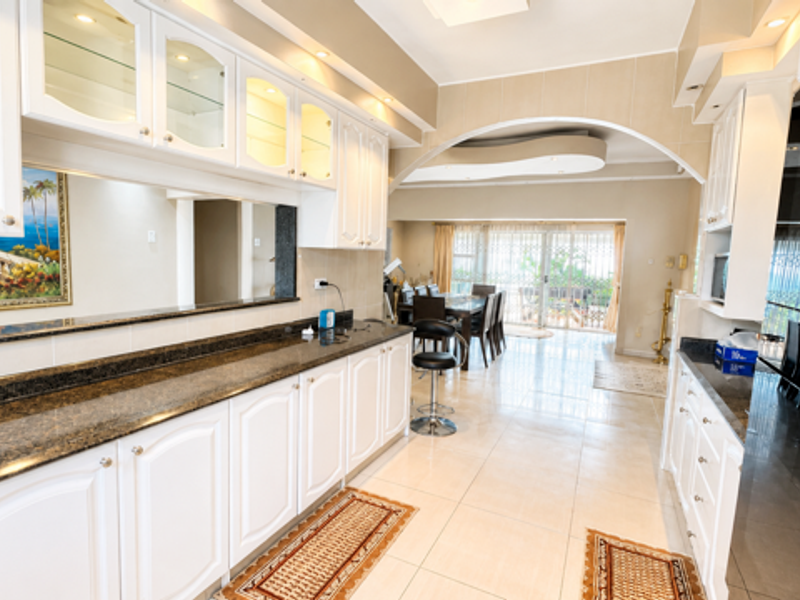 Spacious open-plan kitchen and dining area featuring granite countertops, white cabinetry, recessed lighting, and an elegant archway leading to a bright dining space.
