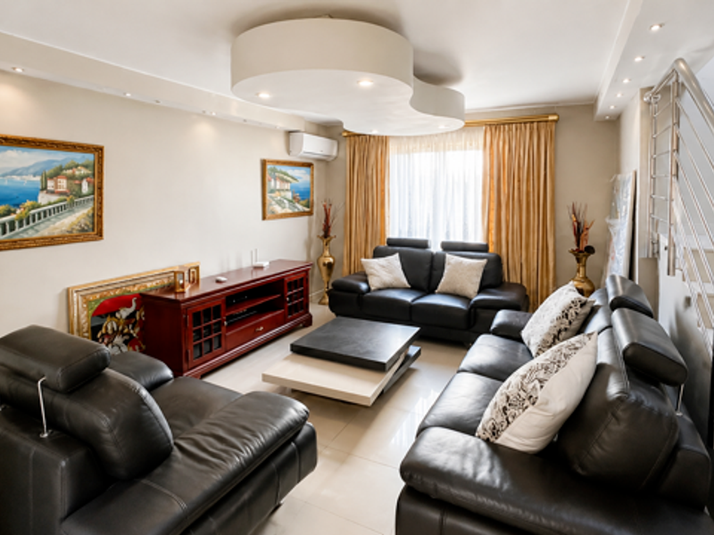A well-maintained living room featuring a unique bulkhead ceiling design, recessed lighting, tiled floors, and a modern staircase with stainless steel railings.